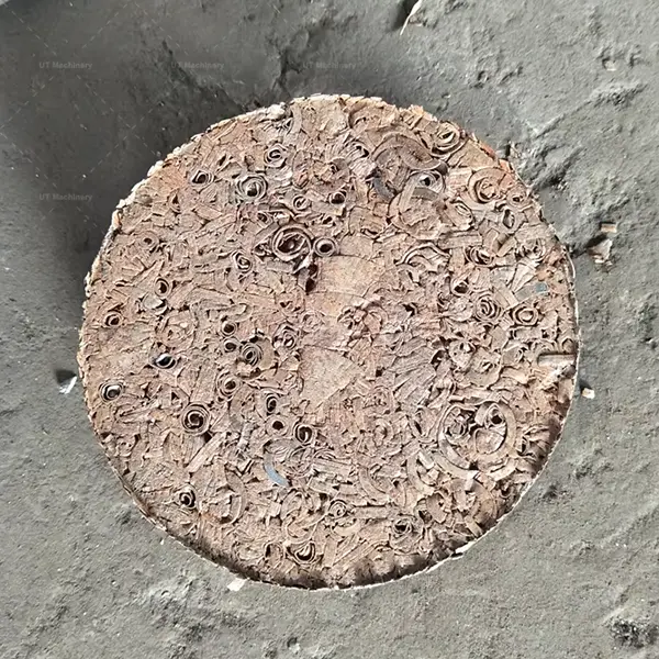 Primer plano cenital de un bloque de briqueta de virutas de latón fuertemente comprimido que muestra una consolidación metálica perfecta.