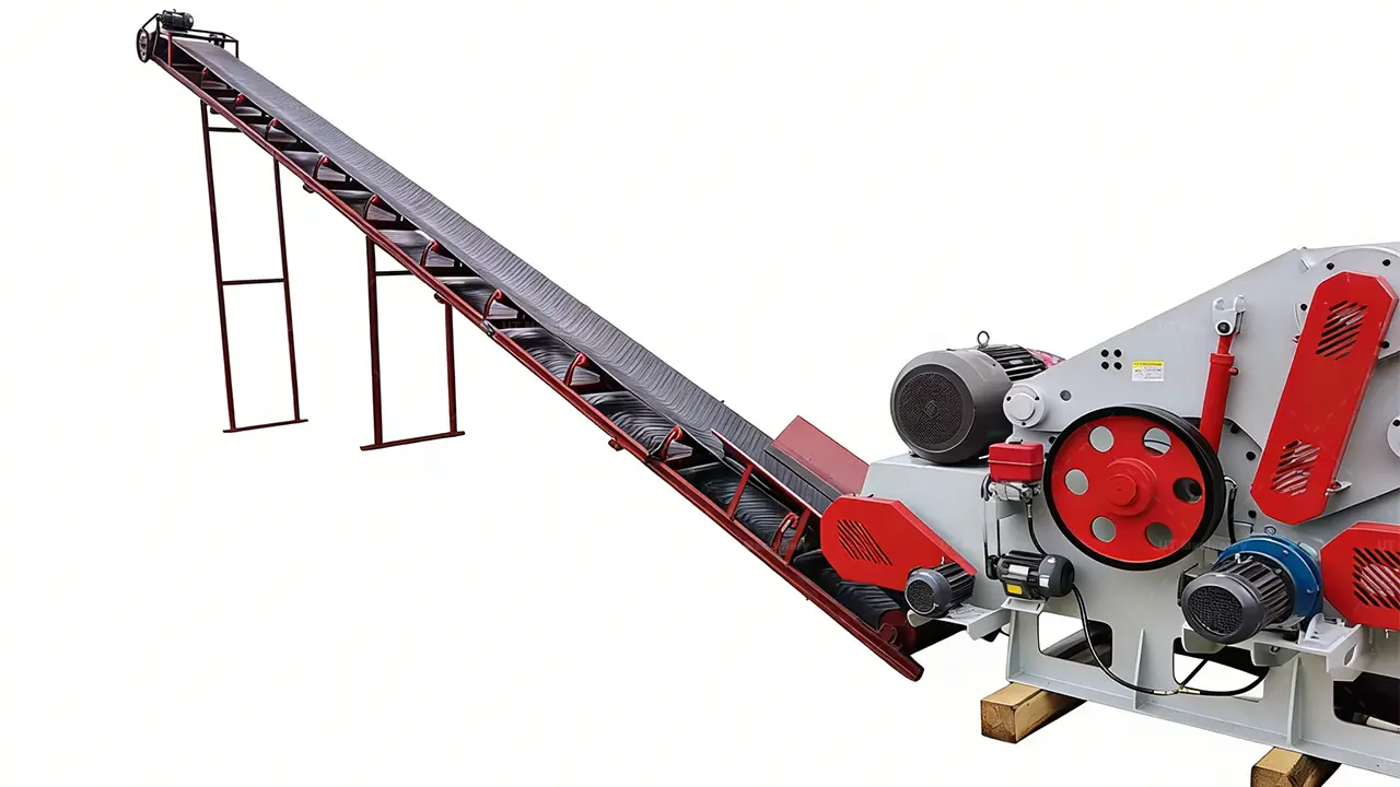Vista lateral detallada de un sistema industrial de astillado de madera, centrada en la conexion entre el largo transportador de alimentacion inclinado y la astilladora de tambor con cuerpo gris, que cuenta con poleas rojas y correas de transmision.